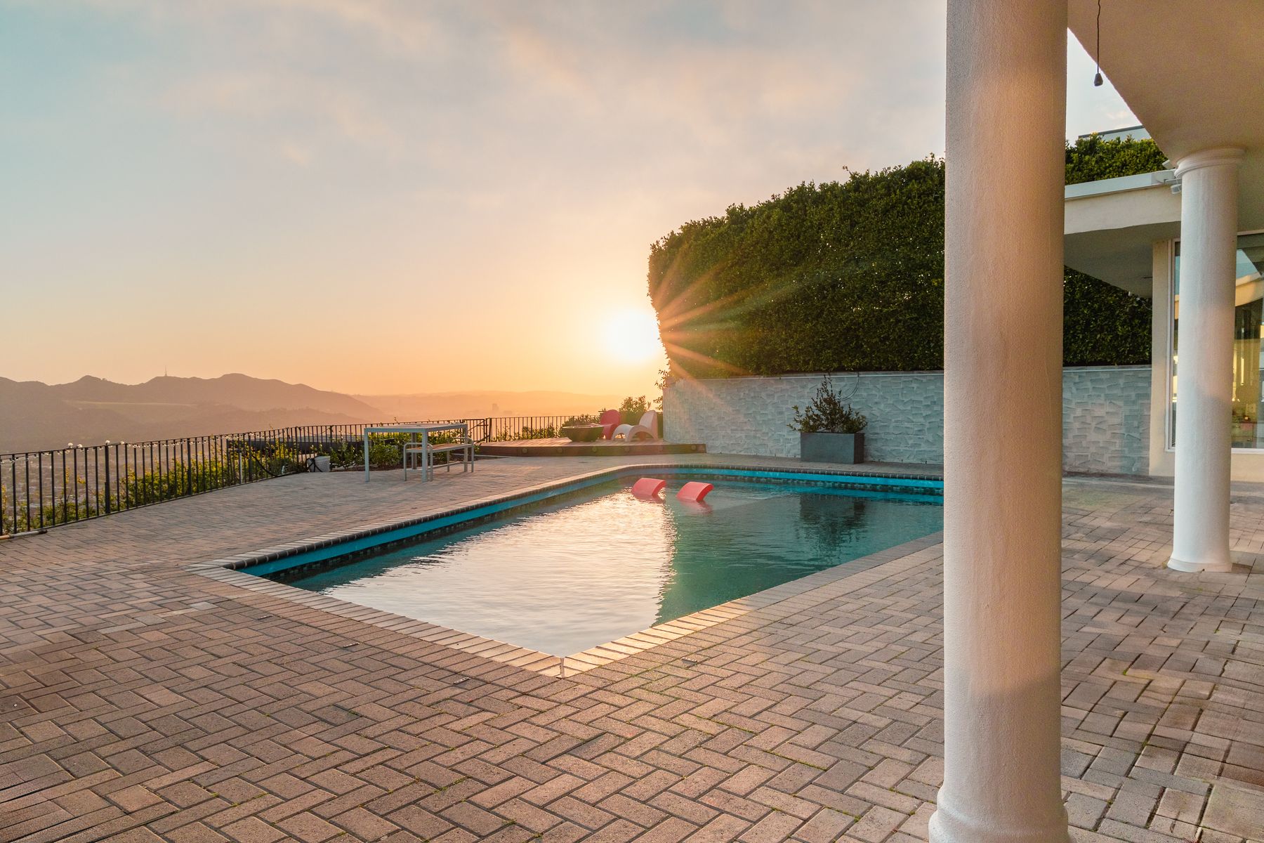 A swimming pool and terrace in the low light of sunset, with hills beyond.