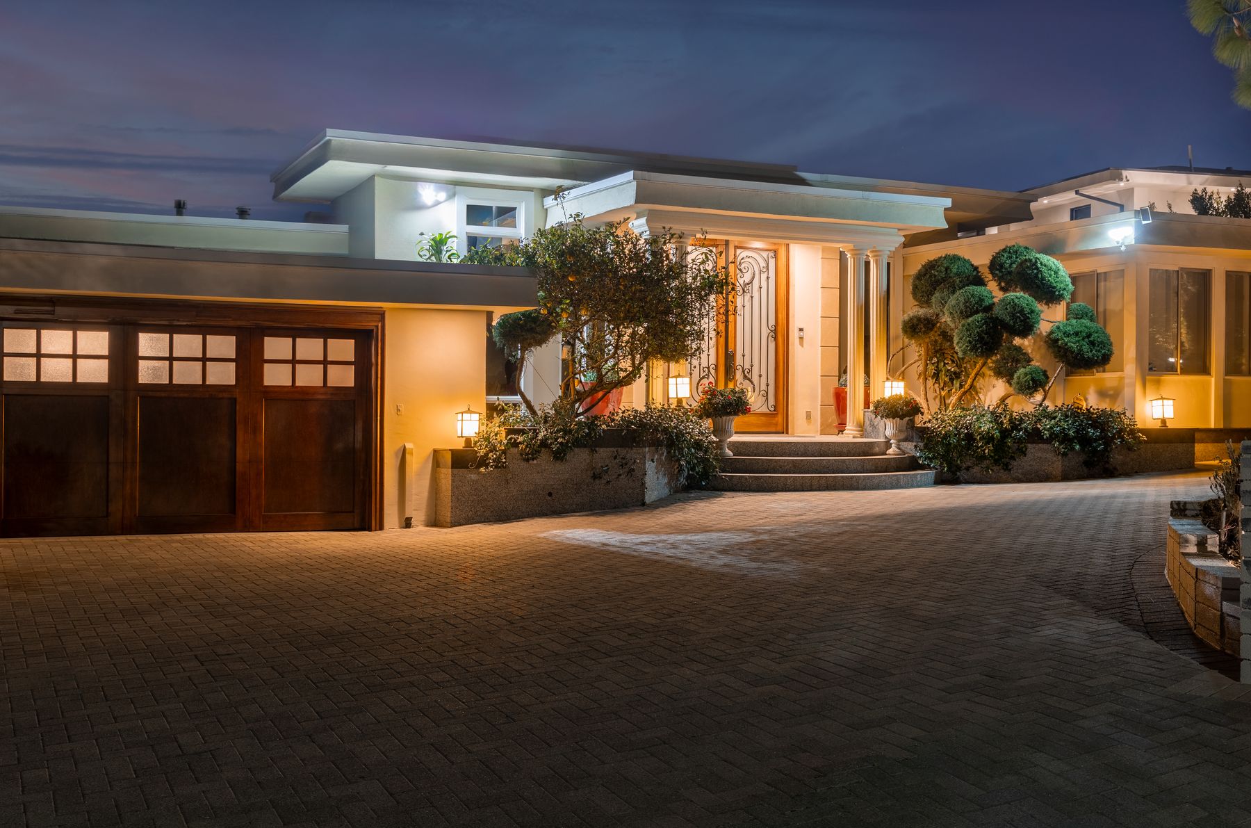 A modern home glowing at dusk, framed by its broad driveway and landscaped entry.