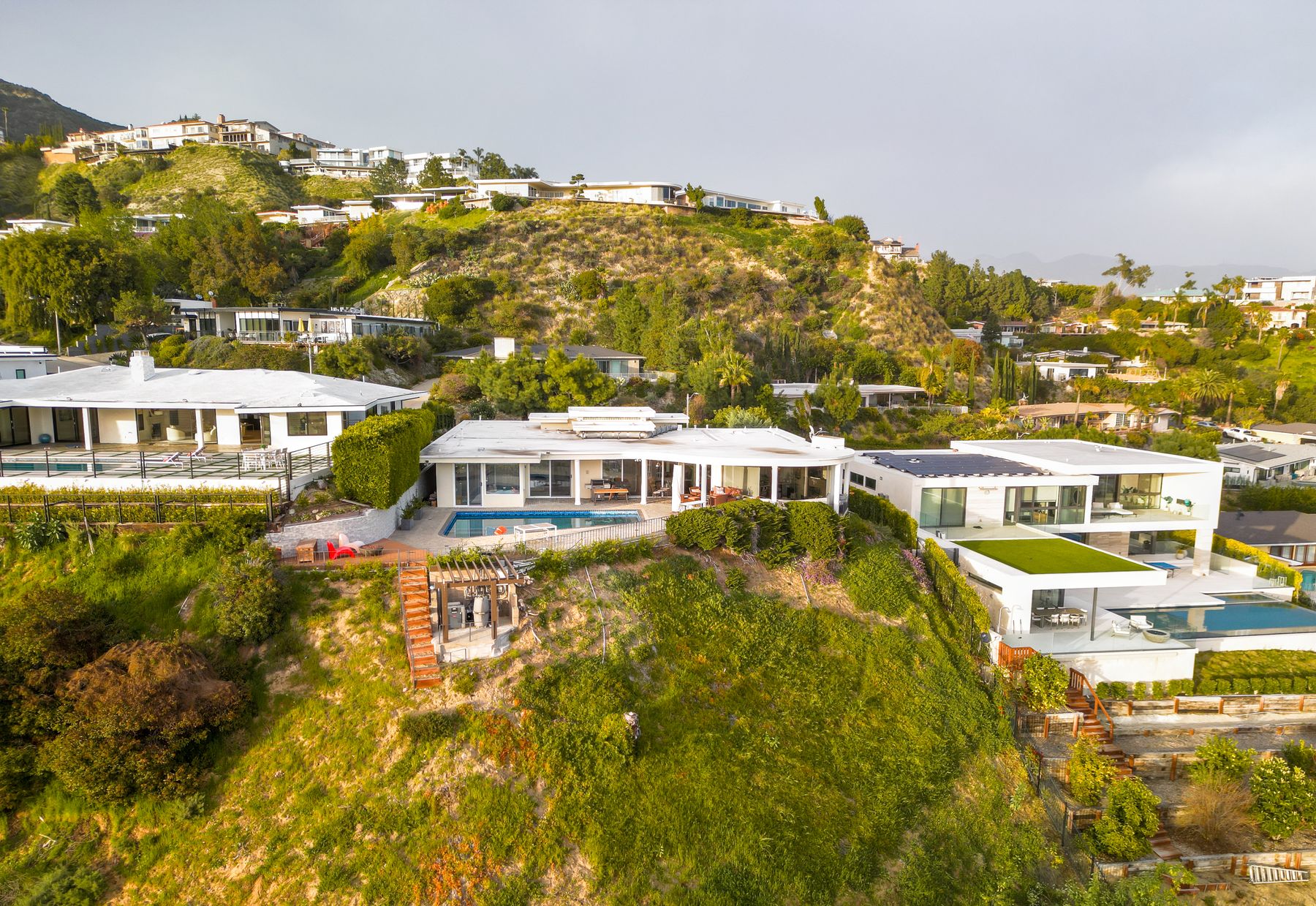 Hillside homes and winding terrain seen from above in clear daylight.