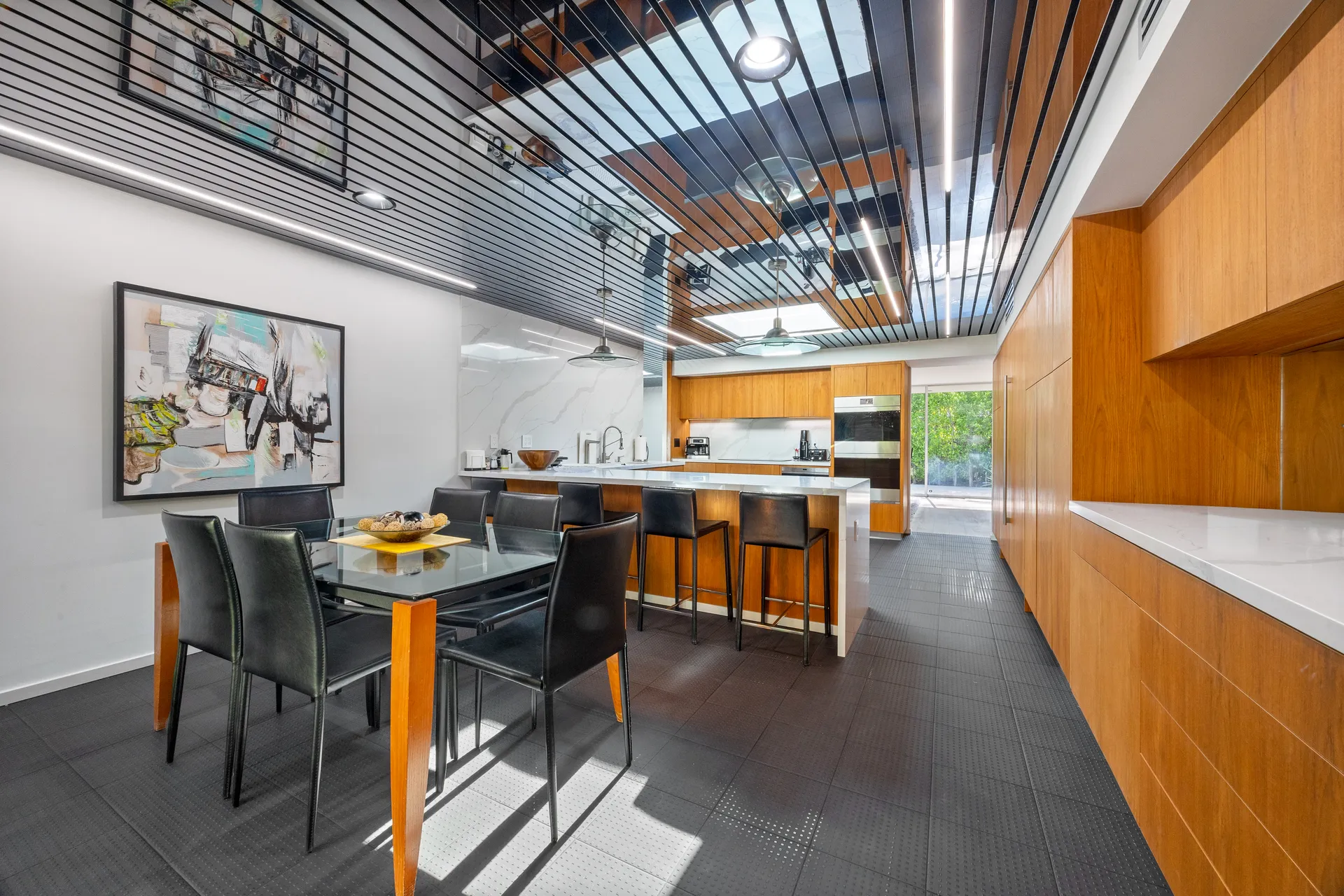 A warm wood kitchen with an island, dark dining chairs, and a reflective slatted ceiling.