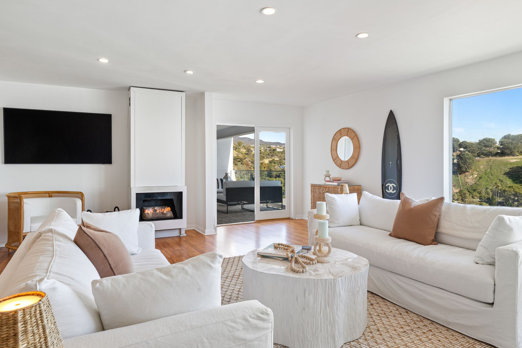A bright living room with generous windows, white furnishings, and a view toward the hills.